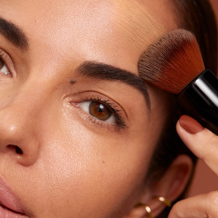 Model applying Skin Long-Wear Weightless Foundation to skin with a foundation brush