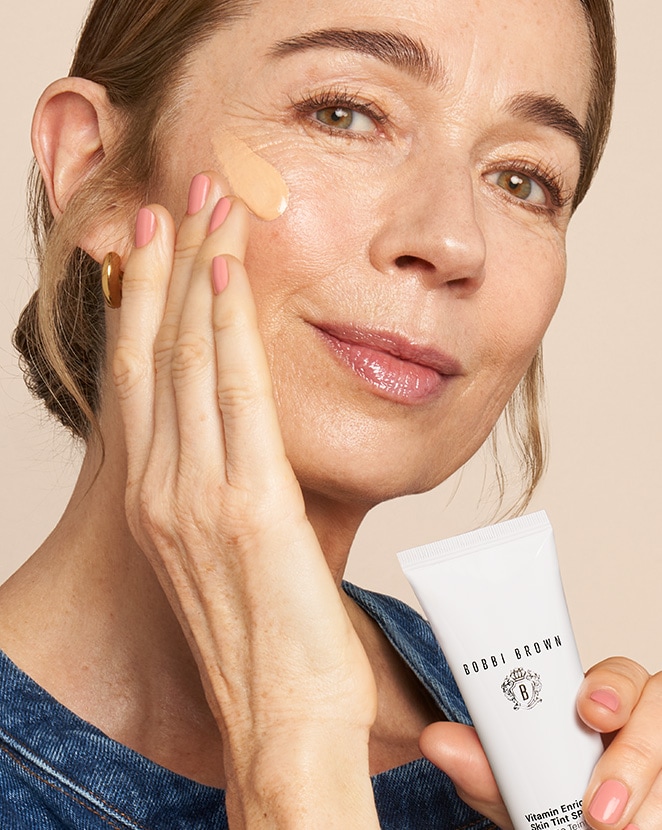 Mature model applying new Vitamin Enriched Skin Tint to skin, with a focus on product texture